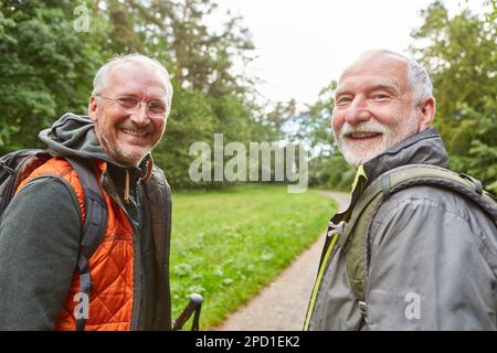 Porträt von glücklichen älteren männlichen Freunden, die Rucksäcke tragen, während sie im Urlaub im Wald wandern Stockfoto