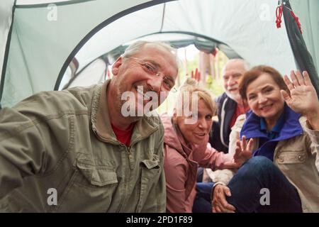 Porträt von glücklichen älteren männlichen und weiblichen Freunden, die winken, während sie Selfie im Zelt machen Stockfoto