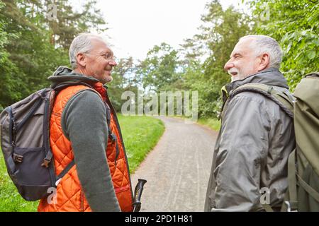 Glückliche ältere männliche Freunde, die Rucksäcke tragen, während sie im Urlaub im Wald wandern Stockfoto