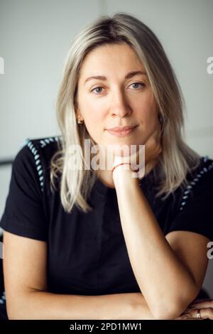 Nahaufnahme des Gesichts einer charmanten 40-jährigen Blondine mit lockerem, geradem Haar, sitzend und in die Kamera blickend. Stockfoto