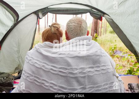 Ein älteres Paar, das während des Waldurlaubs im Zelt saß, in eine Decke gewickelt Stockfoto