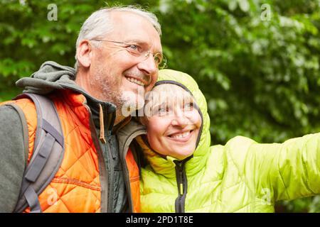 Glückliches älteres Paar in Jacken, das wegblickte, während es im Urlaub im Wald stand Stockfoto