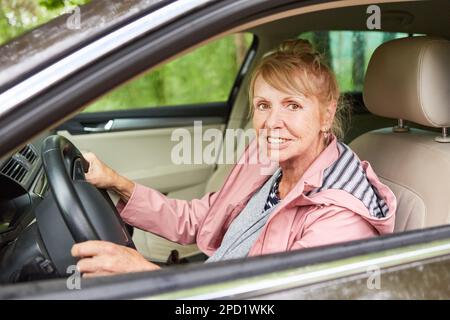 Lächelnde Seniorin, die in der Natur Auto fährt Stockfoto