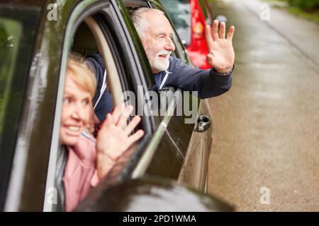 Glückliches Seniorenpaar, das während einer Autofahrt im Urlaub mit den Händen durch die Fenster winkte Stockfoto
