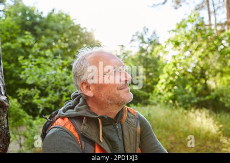 Nachdenklicher Seniorenmann, der während des Urlaubs im Wald lacht Stockfoto