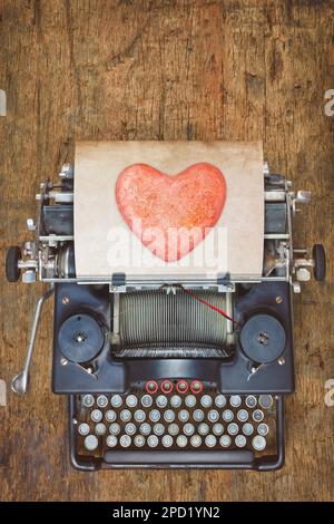 Draufsicht einer alten Schreibmaschine mit rotem Herz auf einem Blatt Papier Stockfoto