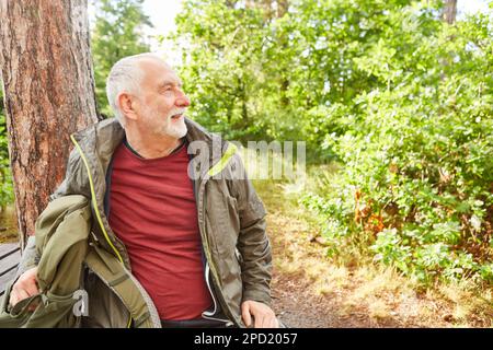 Lächelnder älterer Mann mit Rucksack im Wald während der Sommerferien Stockfoto