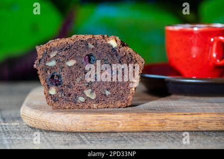 Halber Schokoladen-Muffin mit Blaubeeren und Walnüssen auf einem Holztisch, Nahaufnahme. Süßes Gebäck auf dem Brett. Frische Cupcakes zum Frühstück Stockfoto