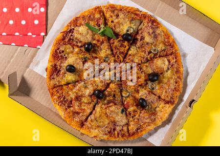 Pizza mit Gemüse und Wurst in einer Pappschachtel für die Heimlieferung auf gelbem Hintergrund, Draufsicht Stockfoto