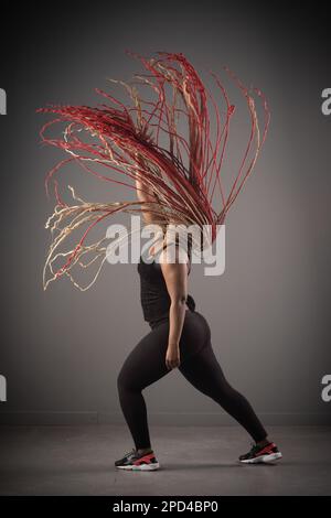 Eine afroamerikanische Frau tanzt fröhlich Hip-Hop mit langen roten Haaren um sie herum Stockfoto