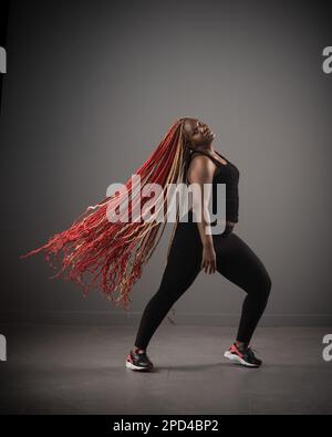 Eine afroamerikanische Frau tanzt fröhlich Hip-Hop mit langen roten Haaren um sie herum Stockfoto