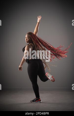 Eine afroamerikanische Frau tanzt fröhlich Hip-Hop mit langen roten Haaren um sie herum Stockfoto