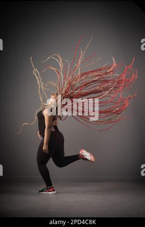 Eine afroamerikanische Frau tanzt fröhlich Hip-Hop mit langen roten Haaren um sie herum Stockfoto