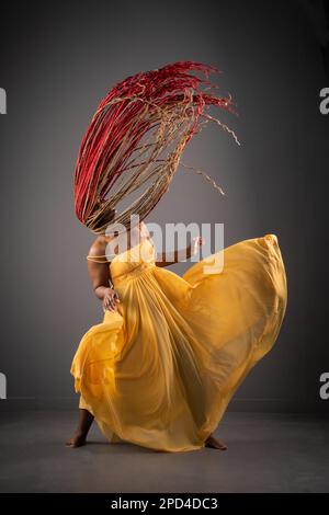 Eine afroamerikanische Frau in einem langen gelben Kleid, die eine energiegeladene Tanzvorstellung zeigt Stockfoto