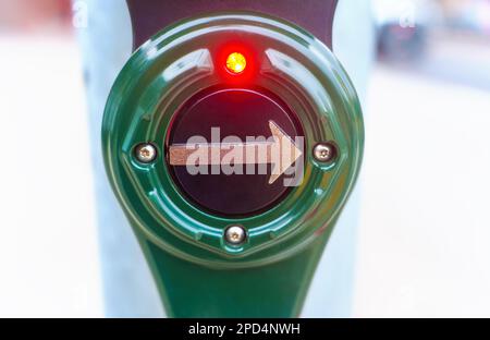 Nahaufnahme einer grünen Fußgängersignaltaste an einem Fußgängerübergang mit leuchtender roter Glühlampe. Stockfoto