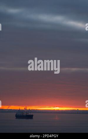 Segelboot und die Sonnenaufgangssonne, die durch eine dicke Wolkenschicht blickt. Stockfoto