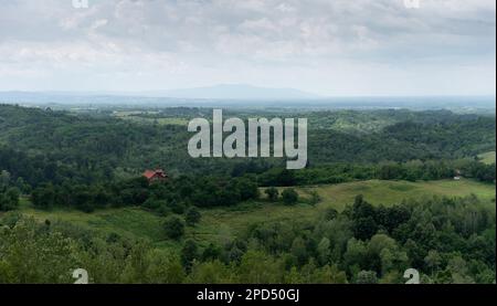 Hügelige Landschaft mit Dörfern an bewölkten Tagen, üppigen Wäldern und trüben Berghängen Stockfoto