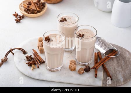 Hausgemachter Chai mit Milch in hohen Gläsern mit Gewürzen auf einem Brett Stockfoto