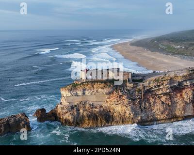 Leuchtturm in Nazare, Portugal. Berühmter Ort für Wellen und Surfen. Strand und Ozeanwellen im Hintergrund Stockfoto