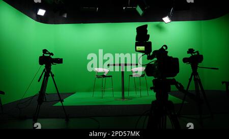 Moderne Einrichtung im Chroma Key Studio mit Fernseher, grünem Bildschirm, Licht, Kameraausstattung und Möbeln. Schießstudio mit Gastgeber und professioneller Ausrüstung. Stockfoto