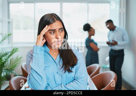 Die junge Frau sieht verärgert aus, während Kollegen hinter ihrem Rücken reden, Bürodrama Stockfoto