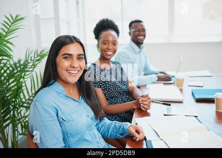 Portrait eines vielseitigen Teams, das am Sitzungstisch in Folge sitzt, junge Frauen Stockfoto
