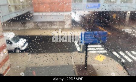 Nahaufnahme von Regentropfen an einem Fenster mit einem sanft verschwommenen Stadtbild dahinter. Atmosphärischer Hintergrund für regnerische Tage, der Stimmung, Wetter, Ruhe und s vermittelt Stockfoto