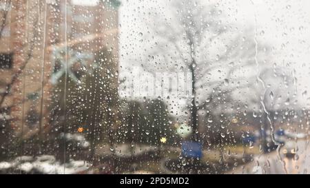 Nahaufnahme von Regentropfen an einem Fenster mit einem sanft verschwommenen Stadtbild dahinter. Atmosphärischer Hintergrund für regnerische Tage, der Stimmung, Wetter, Ruhe und s vermittelt Stockfoto