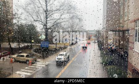 Nahaufnahme von Regentropfen an einem Fenster mit einem sanft verschwommenen Stadtbild dahinter. Atmosphärischer Hintergrund für regnerische Tage, der Stimmung, Wetter, Ruhe und s vermittelt Stockfoto