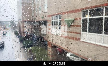 Nahaufnahme von Regentropfen an einem Fenster mit einem sanft verschwommenen Stadtbild dahinter. Atmosphärischer Hintergrund für regnerische Tage, der Stimmung, Wetter, Ruhe und s vermittelt Stockfoto