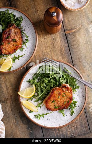 Schweinekoteletts, zubereitet mit Knoblauch, serviert mit Rucola-Salat auf einem Teller Stockfoto