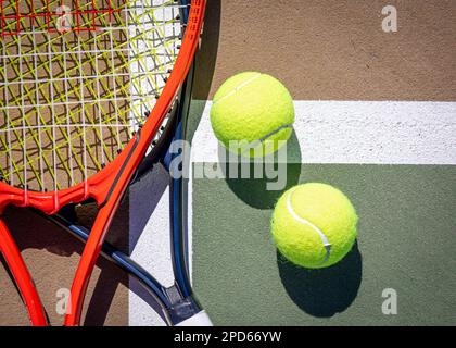 Ein roter und ein blauer Tennisschläger mit zwei Tennisbällen auf der Oberfläche eines Tennisplatzes Stockfoto