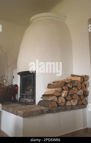 Traditioneller weißer verputzter Holzofen mit einem Haufen Baumstämme in einem Bauernhaus in Ungarn Stockfoto