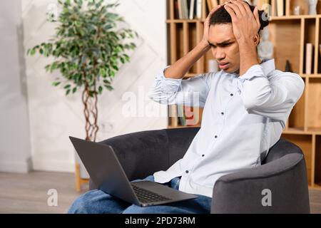 Ein verwirrter, multiethnischer Mann in einem eleganten, lässigen Hemd, der auf den Laptop-Bildschirm schaut, missversteht, was passiert ist, Probleme mit einem Projekt oder Systemfehler auf dem Computer Stockfoto