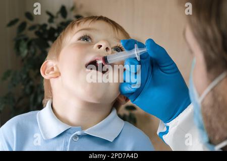 Der Junge bekommt Polio-Tropfen. Arztmachen zum Kind orale Schutzimpfung gegen Infektionen. Kleiner blonder Haarjunge im Krankenhaus. Kindergesundheitsfürsorge und Kinderkrankheiten Stockfoto