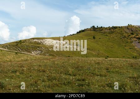 Fantastische Aussicht von unten auf Hügel und Wolken an einem sonnigen Sommertag am Himmel. Gras, Bäume und viele Steine wachsen auf Hügeln. Kleine Steine gießen dow Stockfoto