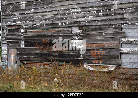 Ein Warnspray, das auf die Seite eines alten verwitterten Holzgebäudes gemalt wurde, um sich fernzuhalten und unbefugtes Betreten zu verhindern. Stockfoto