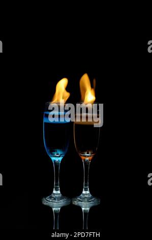 Ein Glas blaues Getränk hinter dem Feuer auf dunklem Hintergrund Stockfoto