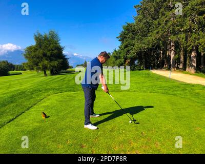 Golfer beim Abschlag auf dem Golfplatz Crans Sur Sierre mit Bergblick in Crans Montana im Wallis, Schweiz. Stockfoto