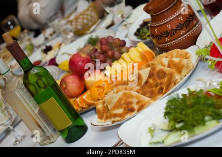 Wunderschöner Banketttisch mit Speisen und Getränken. Wein, Snacks, Obst und andere Speisen stehen auf dem Tisch Stockfoto