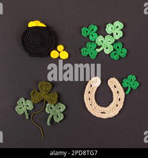 St. Patrick's Day Konzept. Gestrickte Komposition aus einem Topf aus Gold, einem Hufeisen und grünen Shamrocks auf schwarzem Hintergrund Stockfoto