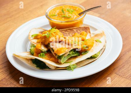 Teller mit veganen Brokkoli Quesadillas, serviert mit einer Aprikosen-Karotten-Sauce. Stockfoto