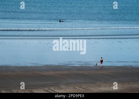 Nicht erkannte Person, die bei Sonnenuntergang am Sandstrand spaziert. Gesunder Lebensstil. Sport im Freien Stockfoto