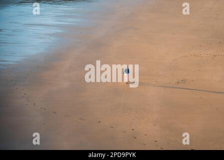 Nicht erkannte Person, die bei Sonnenuntergang am Sandstrand spaziert. Gesunder Lebensstil. Sport im Freien Stockfoto