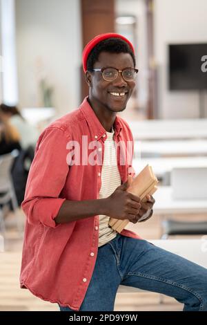 Ein glücklicher, lächelnder, gemischter Schüler mit Brille hält Lehrbücher, zeigt Daumen nach oben Gesten Blick in die Kamera Stockfoto