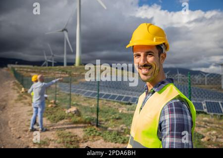Nahaufnahme eines lächelnden Ingenieurs auf einer Solarfarm mit seinen Kollegen im Hintergrund Stockfoto
