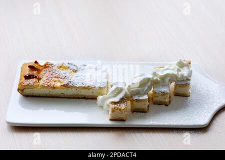 Kondensmilch-Pudding und Eigelb, mit köstlichem Tropfsirup, hausgemacht. Im verschwommenen Hintergrund eine Kaffeekanne und kleine Töpfe mit Zucker, Butter und Zimtpulver. Auf einem Marmortisch Stockfoto