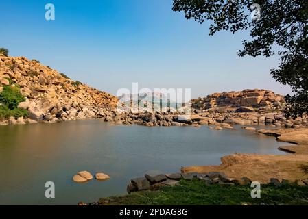 Der Fluss Tungabhadra fließt durch die über Felsen verstreute Landschaft von Hampi. Hampi, die Hauptstadt des Vijayanagara Empire, gehört zum UNESCO-Weltkulturerbe. Stockfoto