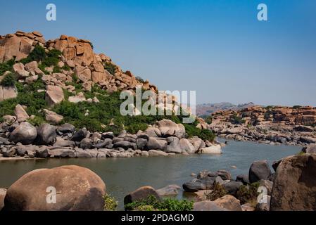 Der Fluss Tungabhadra fließt durch die über Felsen verstreute Landschaft von Hampi. Hampi, die Hauptstadt des Vijayanagara Empire, gehört zum UNESCO-Weltkulturerbe. Stockfoto