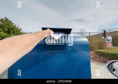 Horizontaler Schuss eines Mannes, der einen Brief in einen Briefkasten steckt. Stockfoto